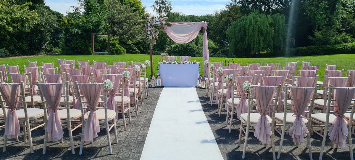 Outdoor ceremony with pink drapes, aisle carpet, gyp pew ends and rustic arch